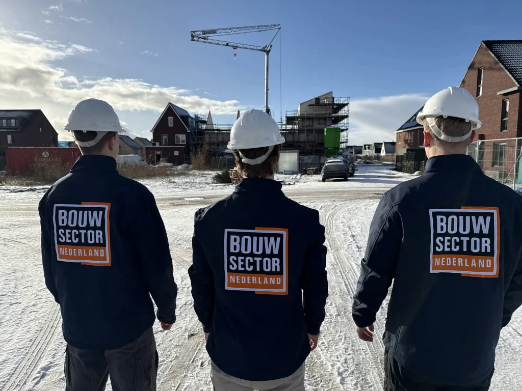 Drie vakmensen van Bouwsector Nederland met witte bouwhelm kijken naar een wijk in aanbouw